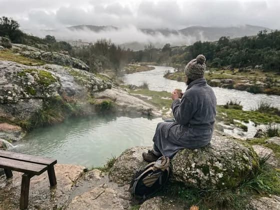 Persona en albornoz y gorro de lana sentada en una roca junto a una poza (imagen ilustrativa generada por IA)